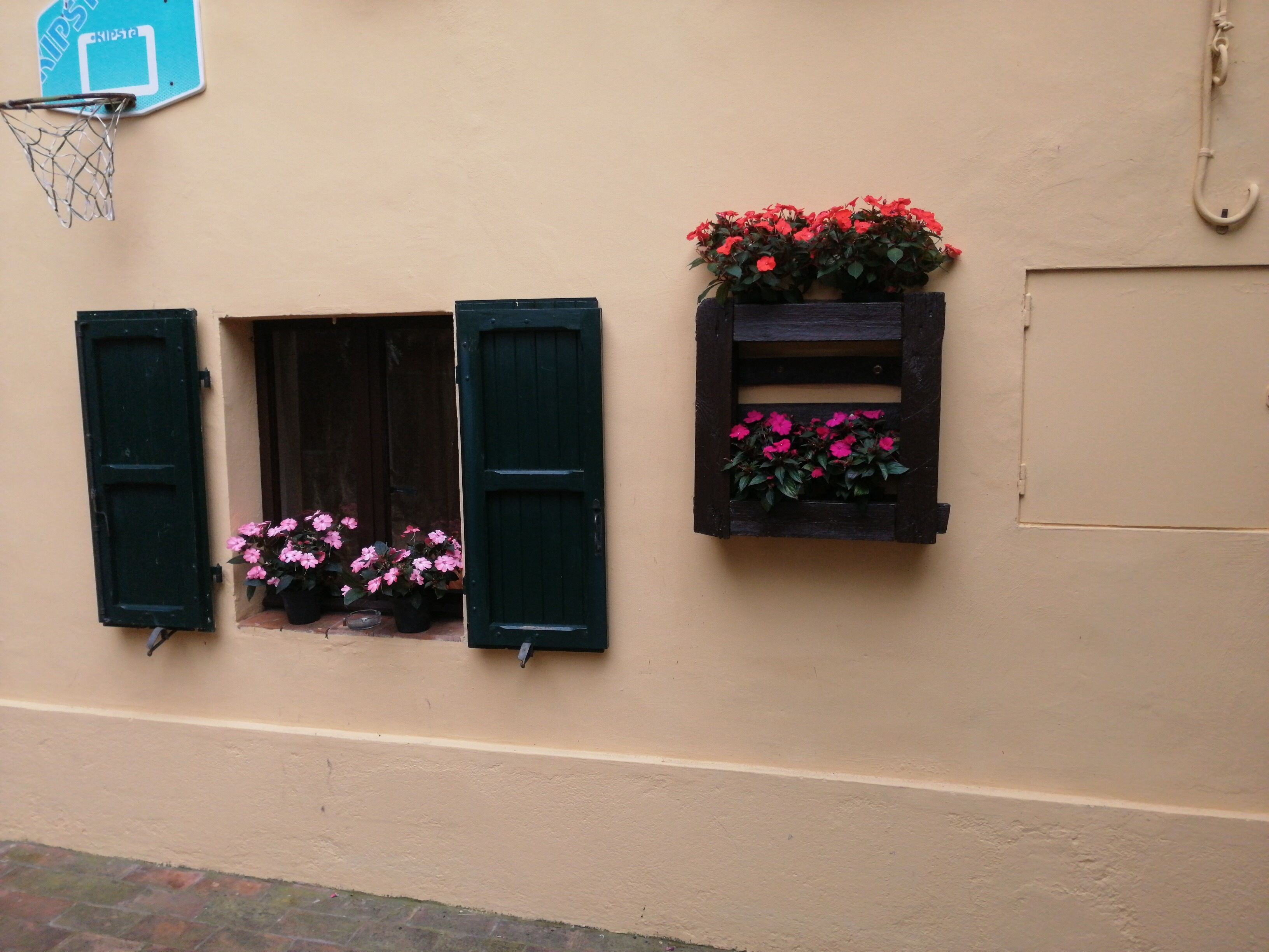 A building with two windows, one with open shutters and a flower box, and another with closed shutters and a flower box.