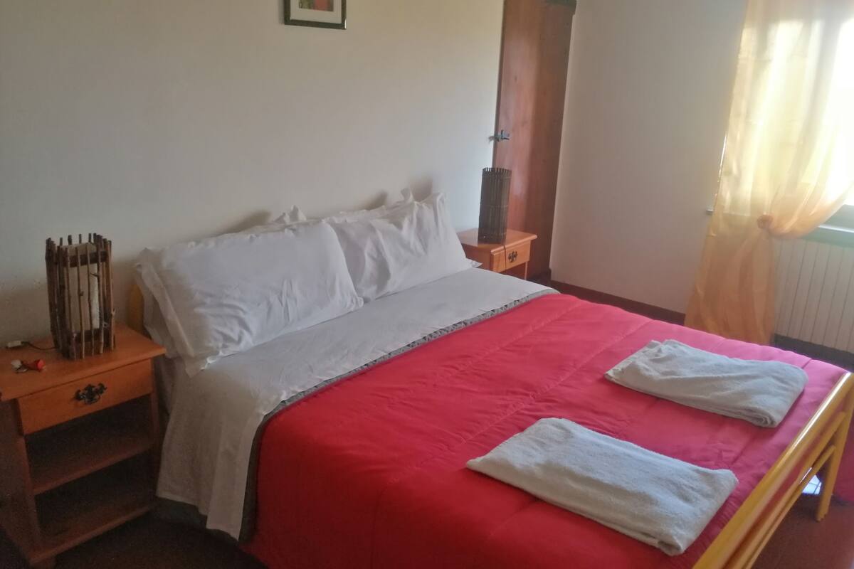 A bed with a red bedspread, white pillows, and two white towels folded on it.