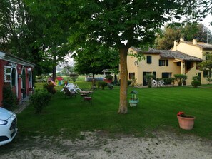 A courtyard with a lawn, outdoor furniture, and a white car parked on the side. - La Valle Del Poeta (Castelfidardo)