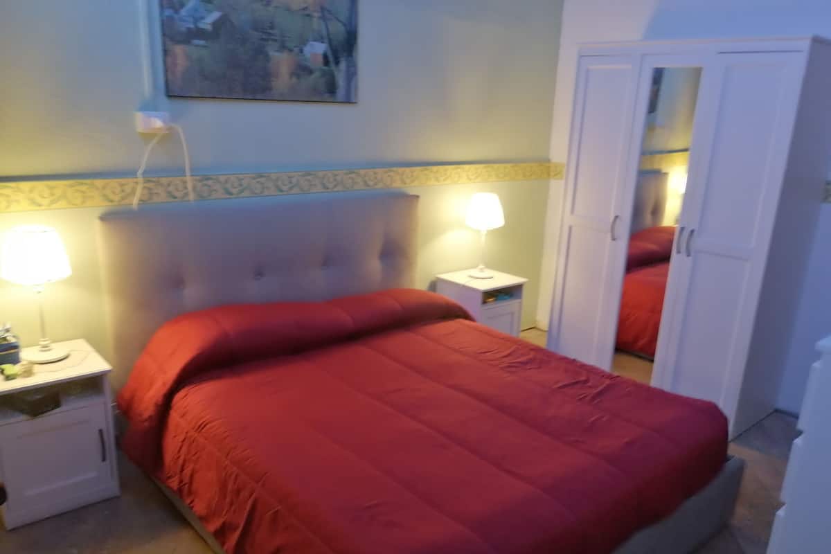 A bedroom with a bed, two bedside lamps, a nightstand, a wardrobe, and a painting on the wall.
