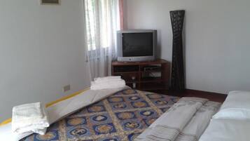 Una habitación de hotel con una cama, un televisor sobre un soporte de madera y una ventana con cortinas.