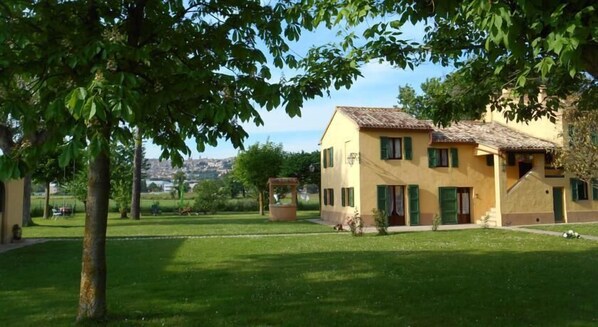 A yellow building with green shutters, a well-maintained lawn, and a pergola in the foreground. - La Valle Del Poeta (Castelfidardo)