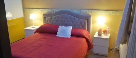 Une chambre d’hôtel avec un grand lit, deux tables de chevet, une petite table, un tableau accroché au mur et une bordure décorative sur le mur.