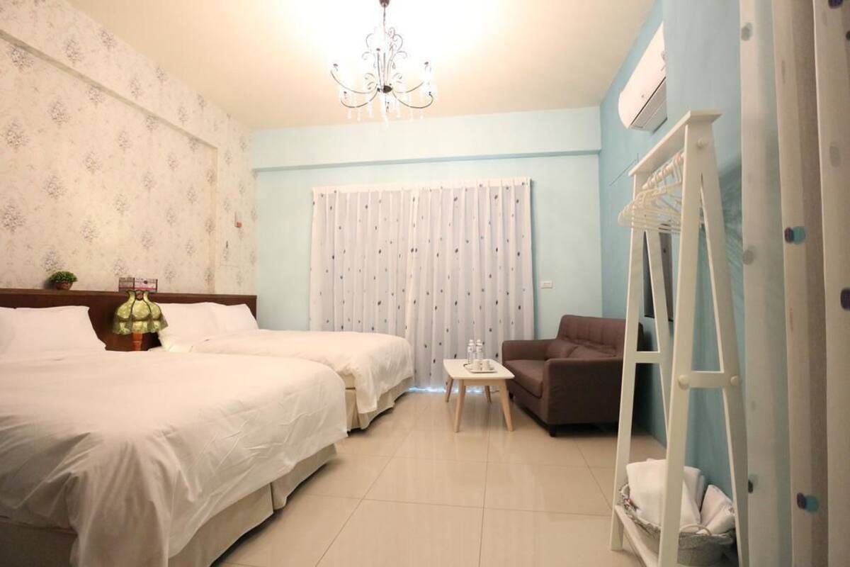 A hotel room with two beds, a small table, a sofa, a chandelier, and a white wardrobe.