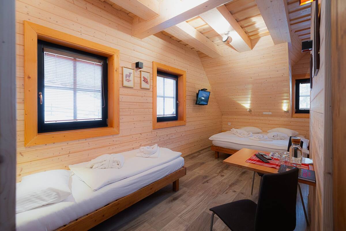 Ein gemütliches Blockhaus mit zwei Holzbett, einem kleinen Tisch mit Stuhl und einem an der Wand befestigten Fernseher.