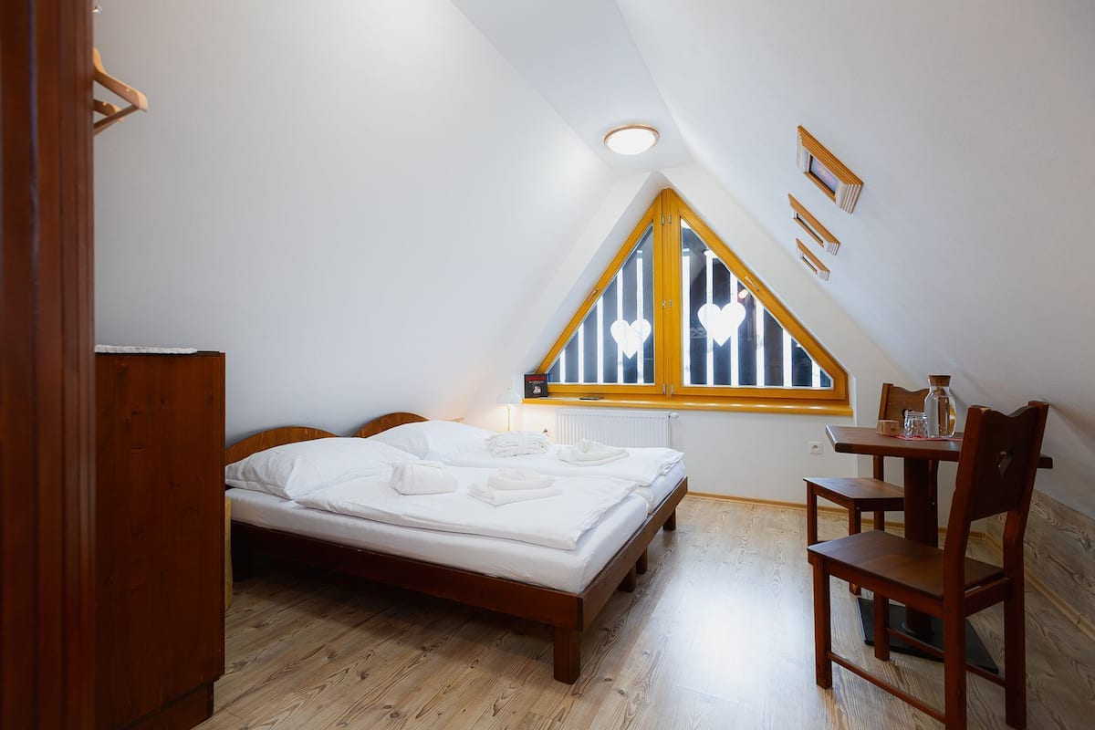 Ein Schlafzimmer mit einem Holzbett, einem kleinen Tisch mit Stühlen, einem Fenster mit Holzrahmen und einer Heizung.