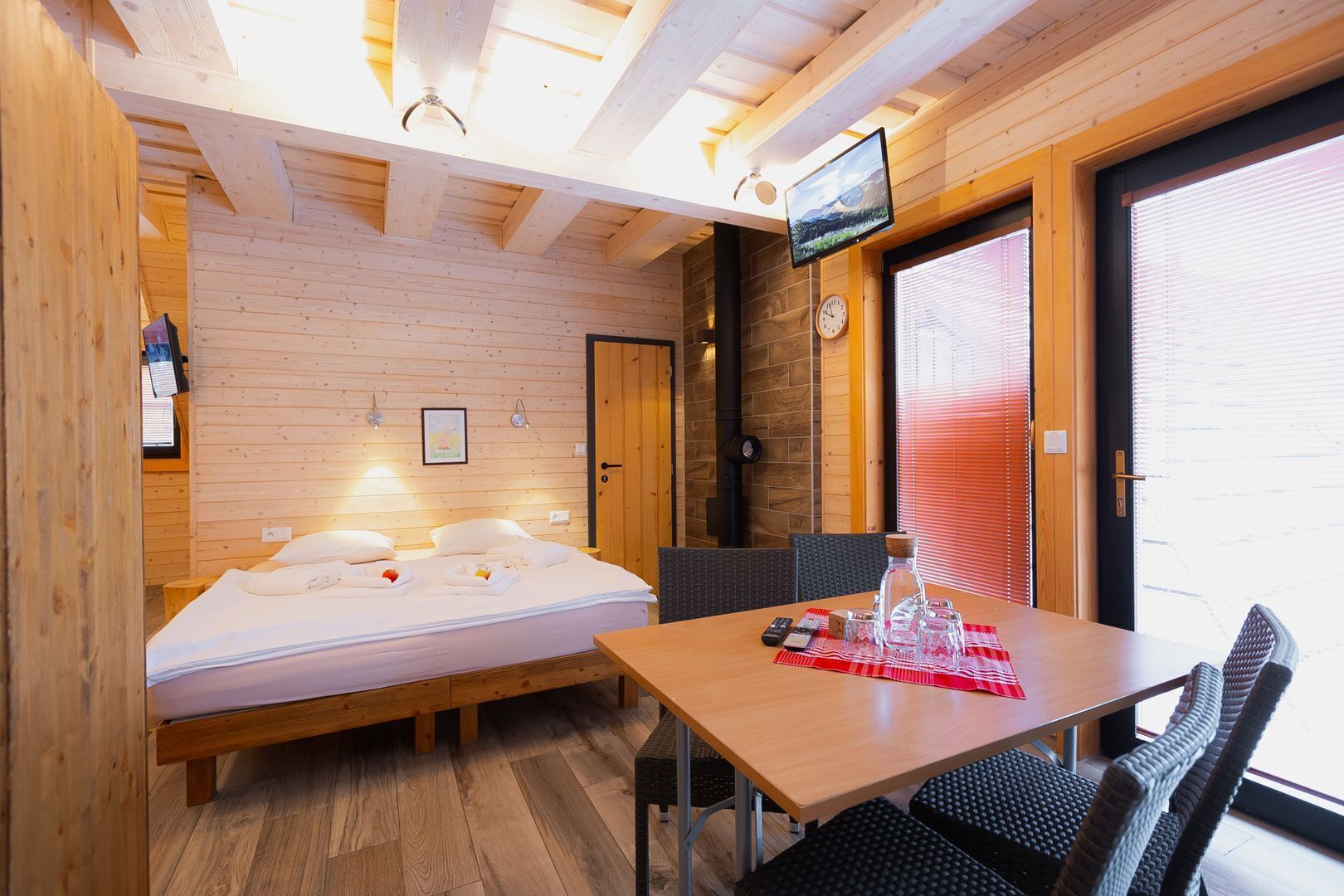 Ein gemütliches Zimmer mit einem Bett, einem Tisch mit Stühlen, einem Fernseher und einem Fenster mit Jalousien.