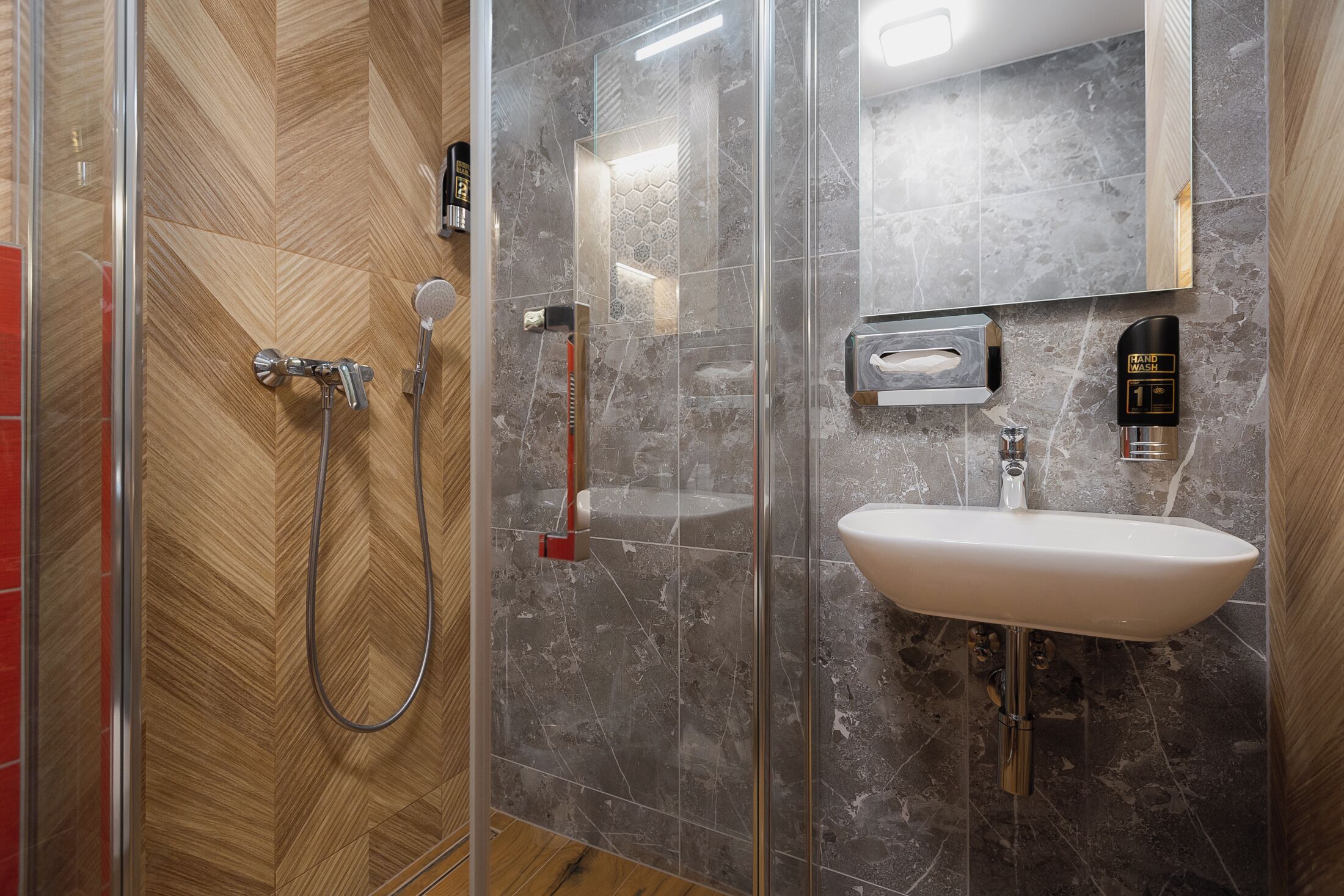 A modern bathroom with a glass shower enclosure, a white sink, and a marble-tiled wall.
