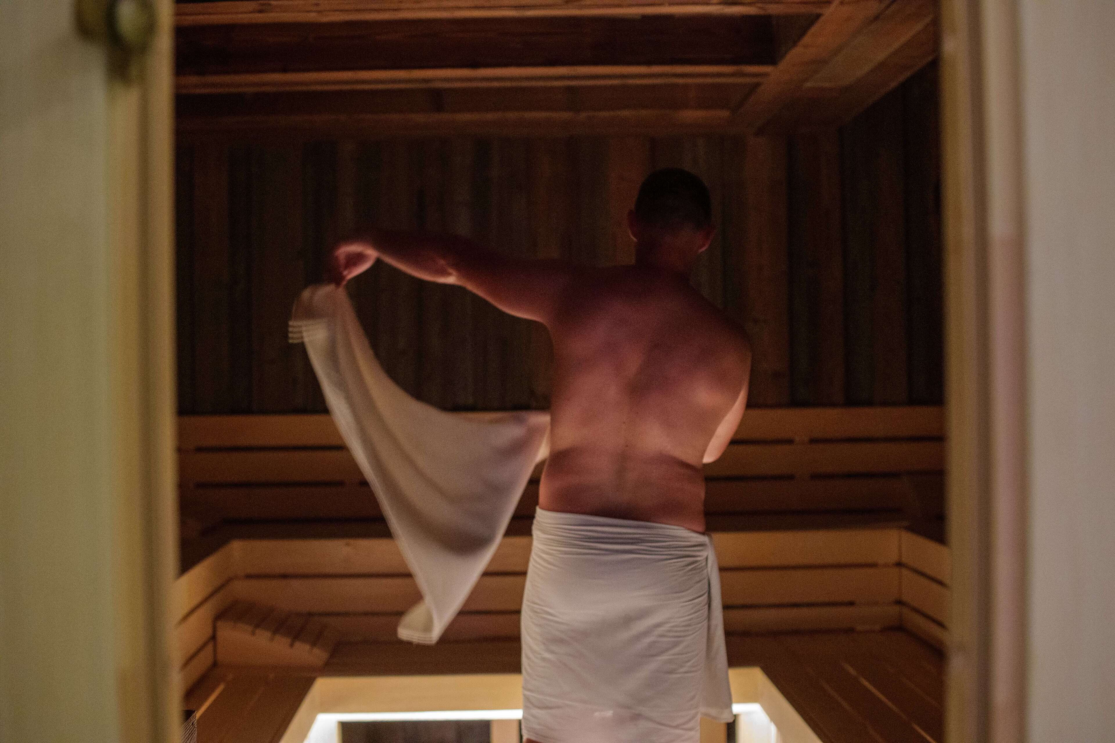 A person in a wooden sauna room, holding a towel.