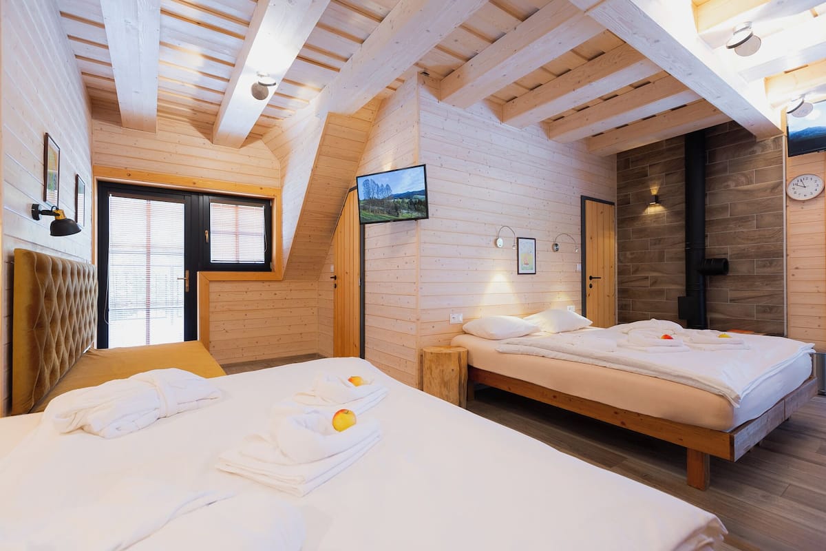 Ein gemütliches Zimmer mit zwei Betten, Holzwänden, einem großen Fenster und einem Fernseher.