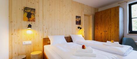 A hotel room with two beds, wooden panel walls, artwork, and a window.
