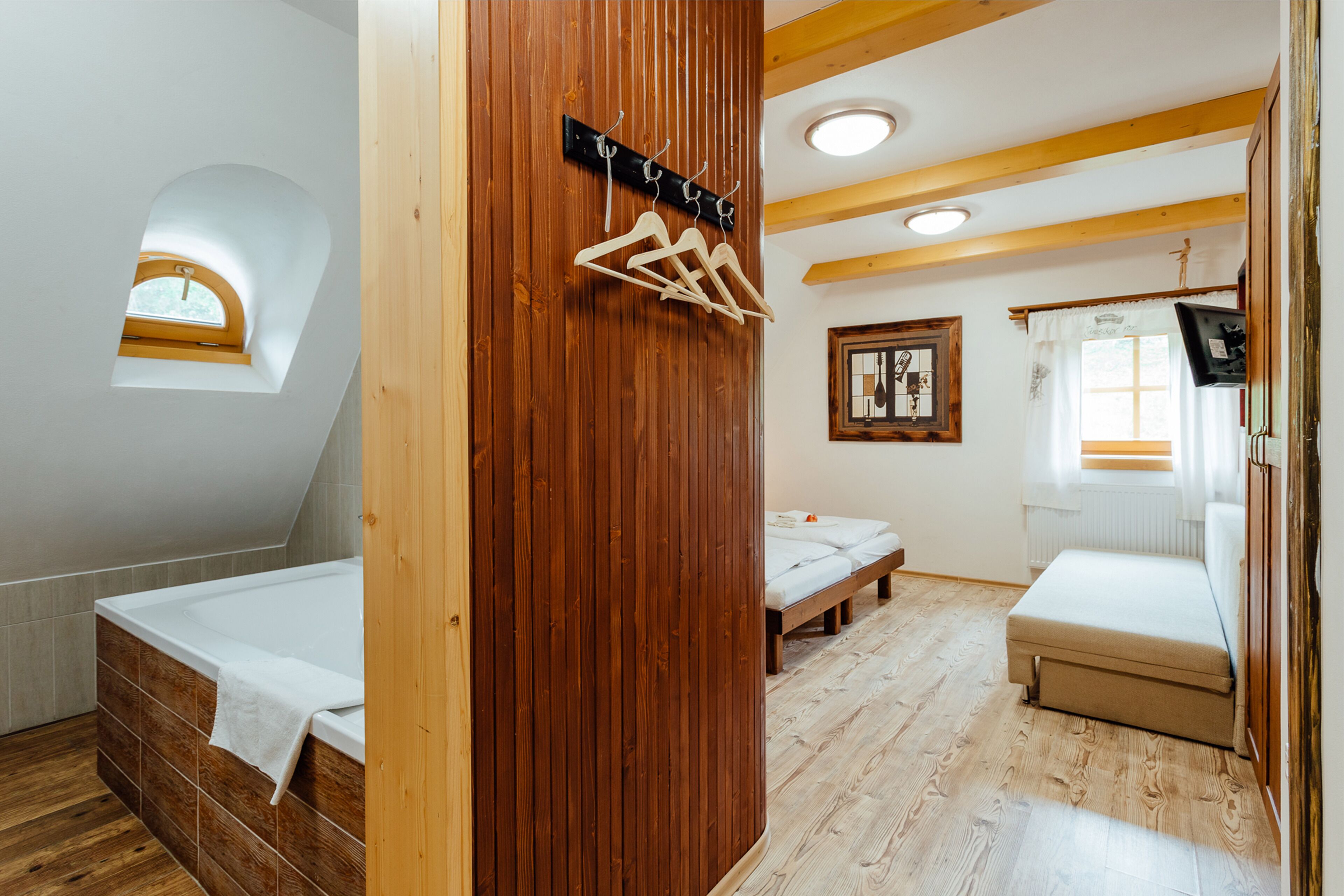 A bedroom with a wooden floor, a loft bed, a small window, and a wooden wall with a coat rack.