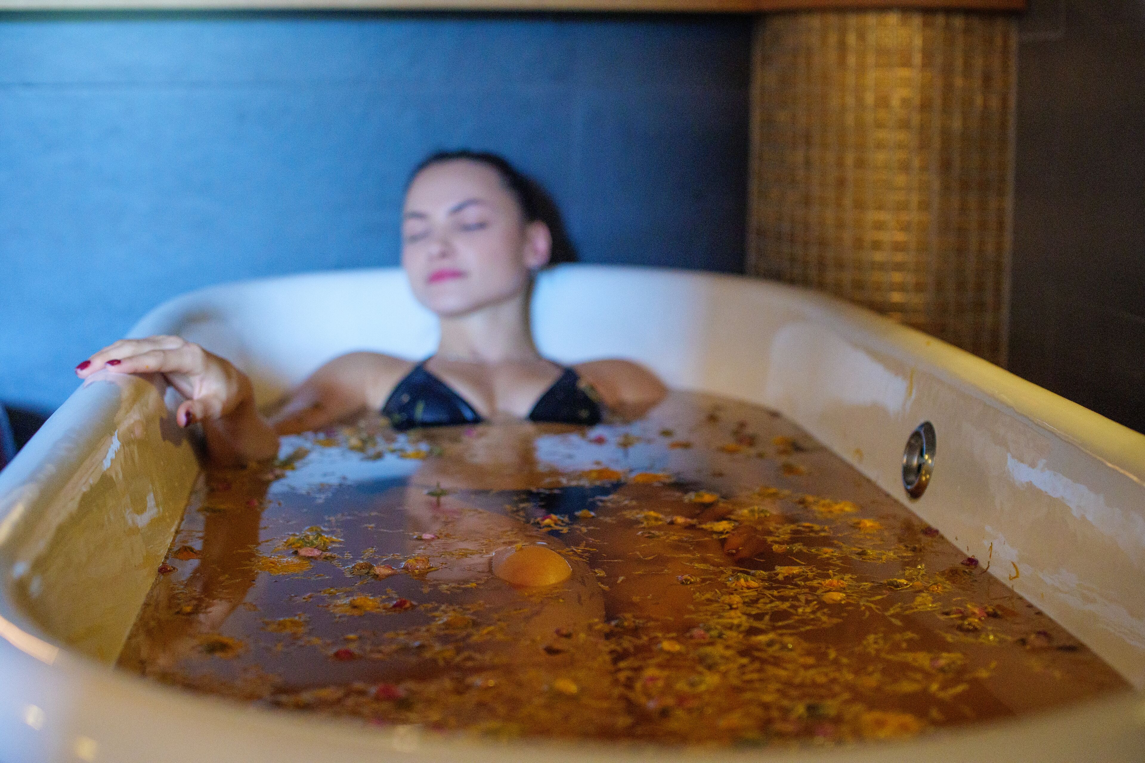 A person in a bathtub filled with water and rose petals.