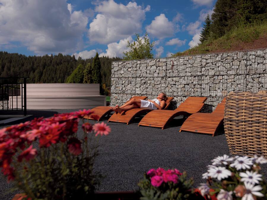 Un muro de piedra con una terraza de madera y sillones de descanso.