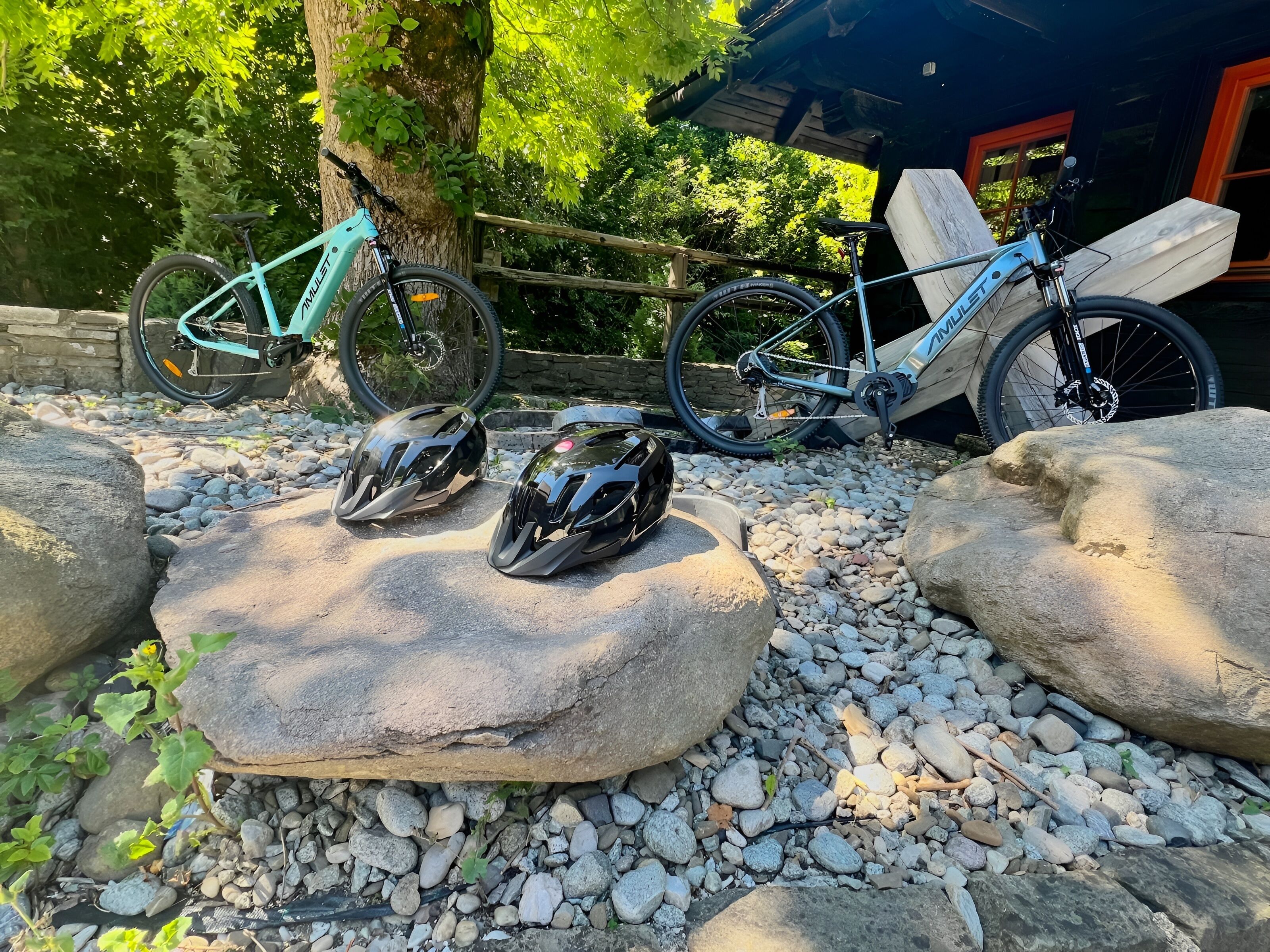 Dos bicicletas estacionadas cerca de una estructura de madera con un muro de piedra y un árbol de fondo.