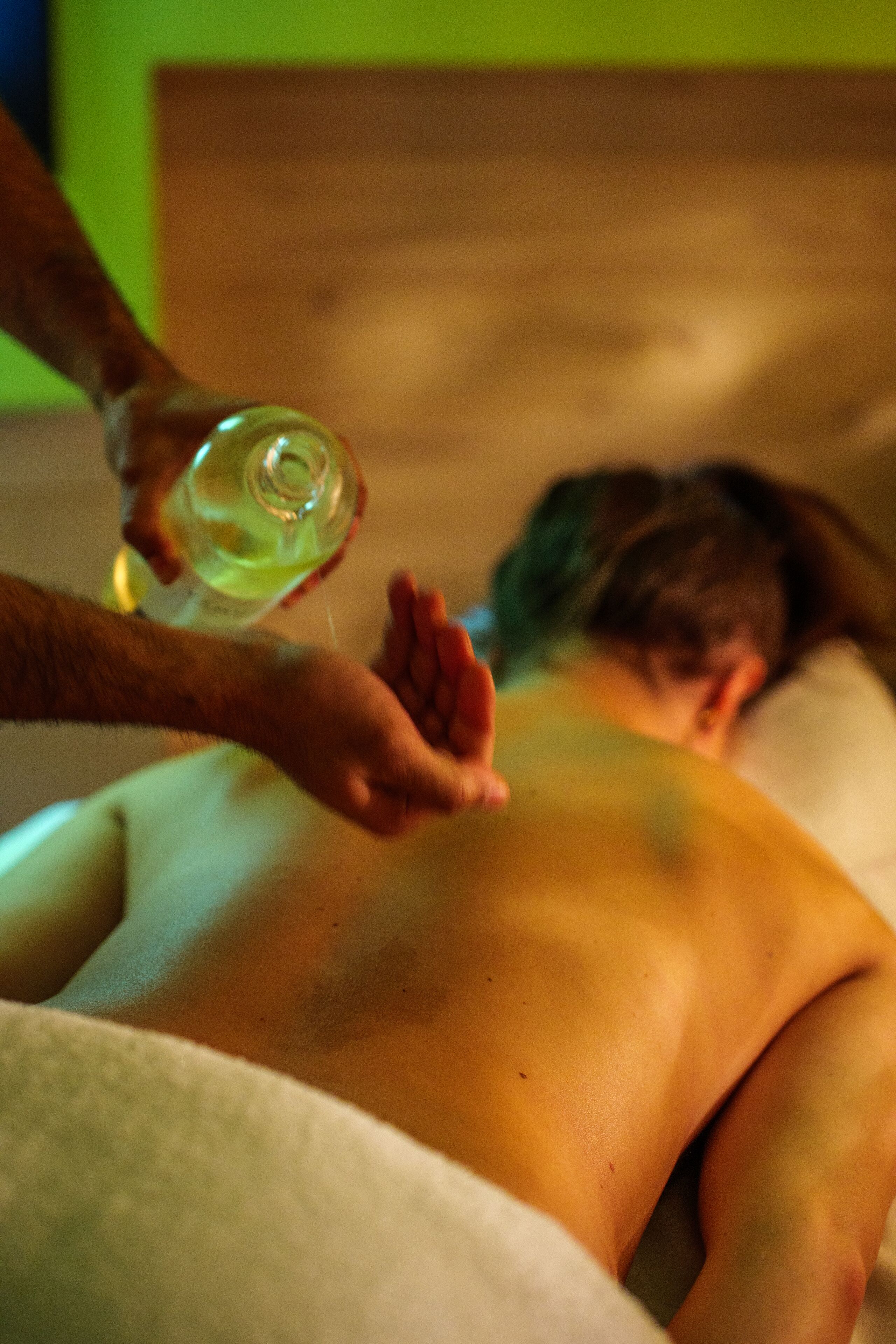 A person receiving a back massage with a bottle of oil.