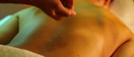 A person receiving a back massage with a bottle of oil.