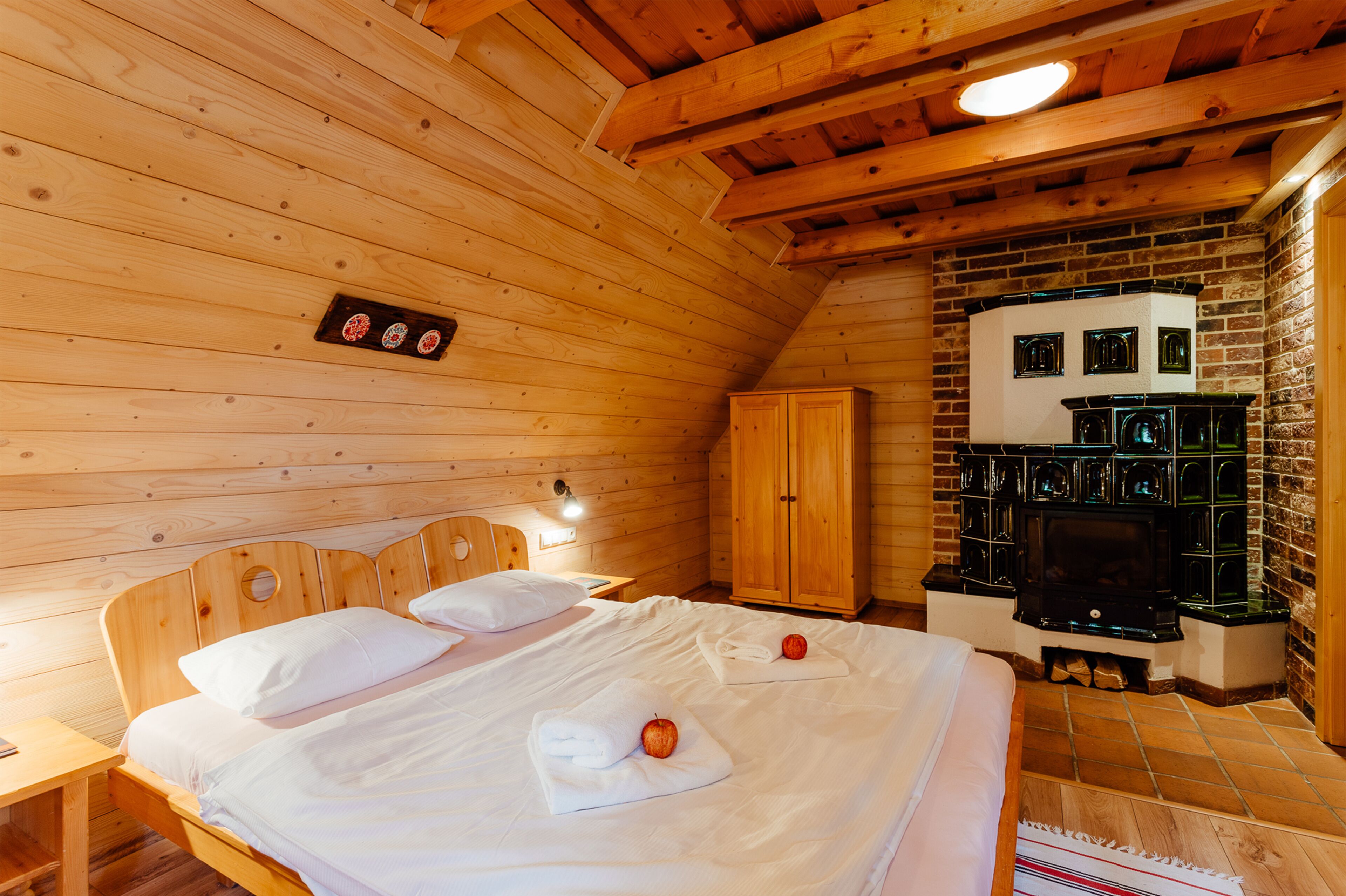 Une chambre dans une cabane en bois, avec un lit, une tête de lit en bois, une armoire, une cheminée et une petite étagère fixée au mur.