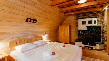Une chambre dans une cabane en bois, avec un lit, une tête de lit en bois, une armoire, une cheminée et une petite étagère fixée au mur.