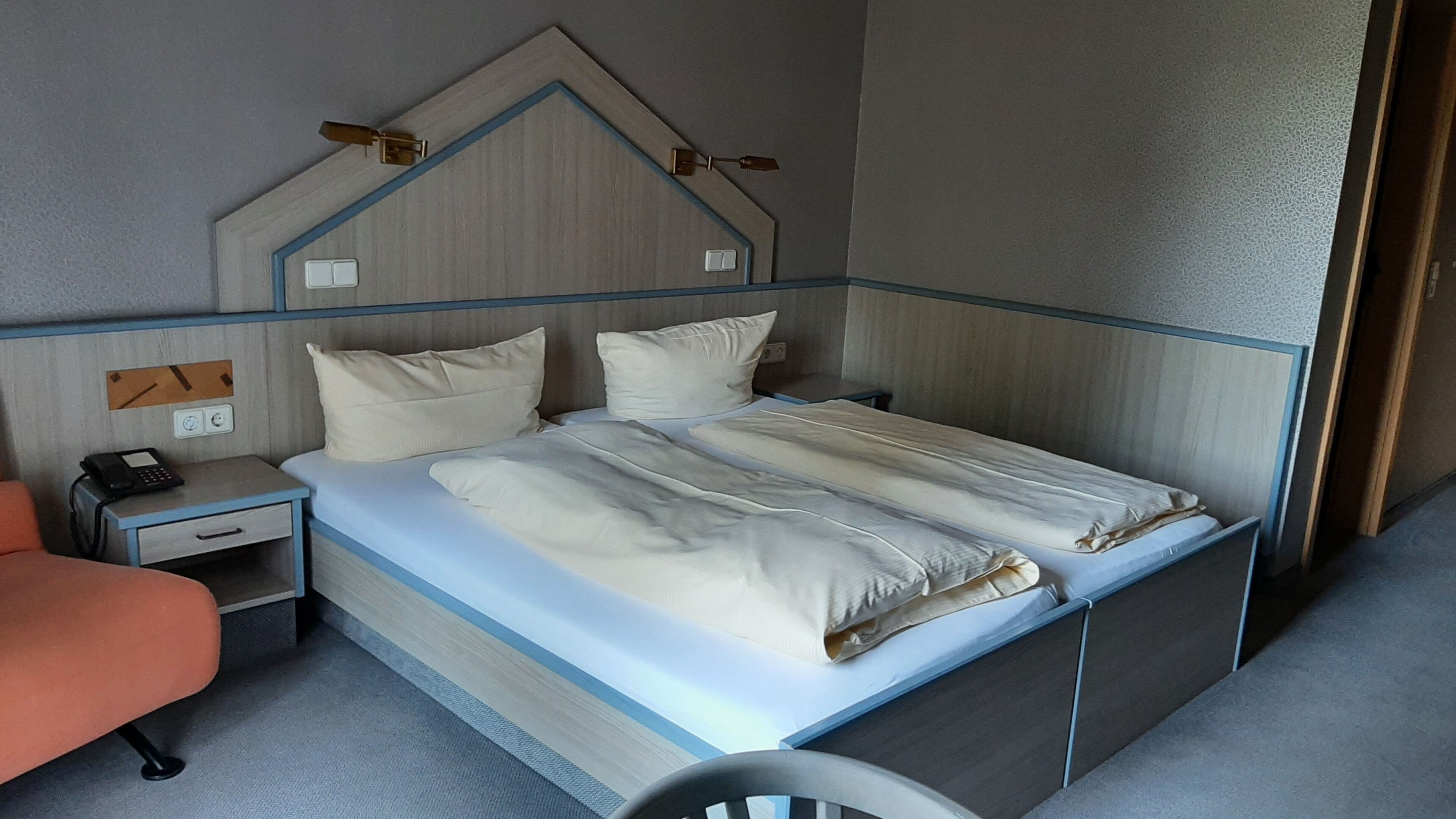 A single bed with a headboard, a bedside table with a phone, and a chair.