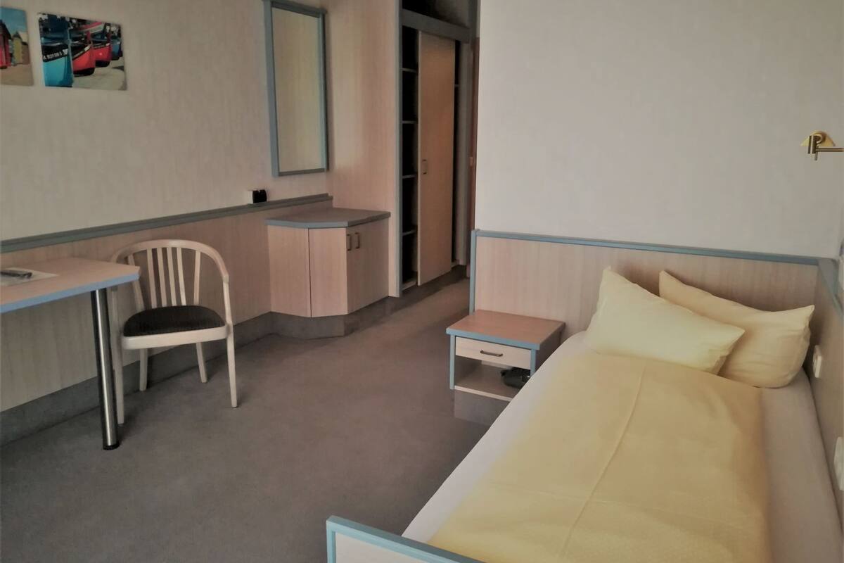 Une chambre à coucher comprenant un lit, un bureau, une chaise, une petite table de chevet et une armoire.