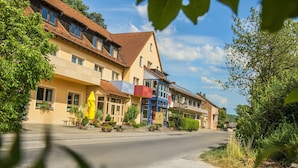 Uma fileira de edifícios tradicionais em estilo europeu, com varandas, uma rua à frente e vegetação nas laterais.