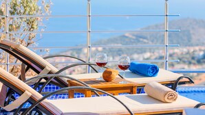 A sunlit terrace with a pool, two lounge chairs, a table with a towel and two glasses of red wine, and a view of the sea and hills. - Villa Gelincik-Hill Villas Kalkan (Kas)