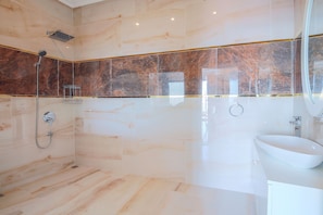 A modern bathroom with a marble shower, a white sink, and a large mirror.