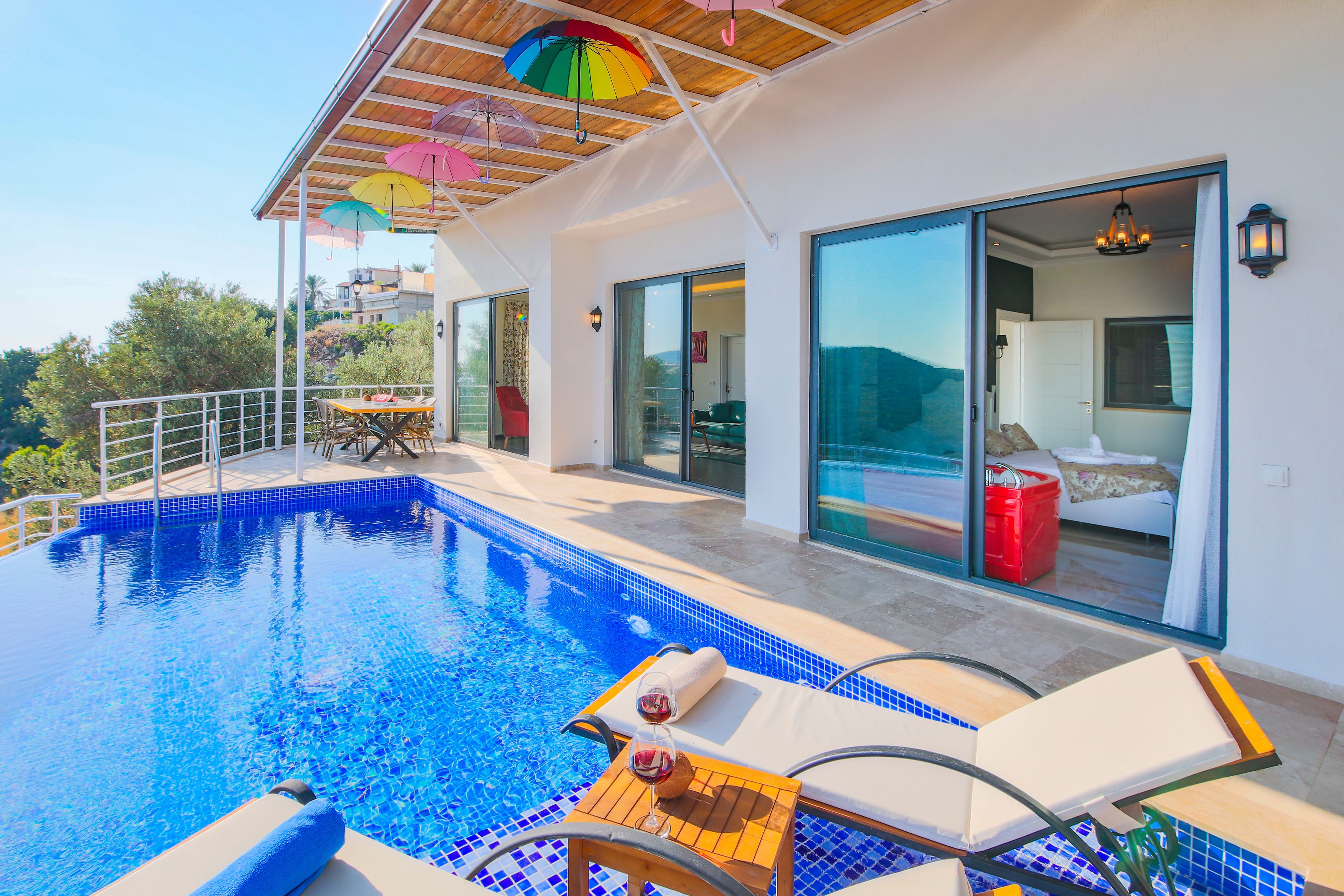 Ein moderner Poolbereich mit klarem, blauem Pool, Liegestühlen und einem Holztisch mit einem Weinglas.