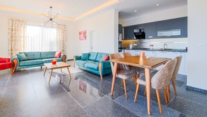 A modern living room with a sofa, a dining table, and chairs. There is a kitchen area with cabinets and appliances. - Villa Gelincik-Hill Villas Kalkan (Kas)