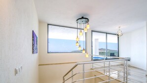 A modern interior with a staircase, large windows, and a hanging light fixture.