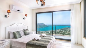 A bedroom with a large bed, two bedside lamps, an air conditioning unit, and a view of the sea.