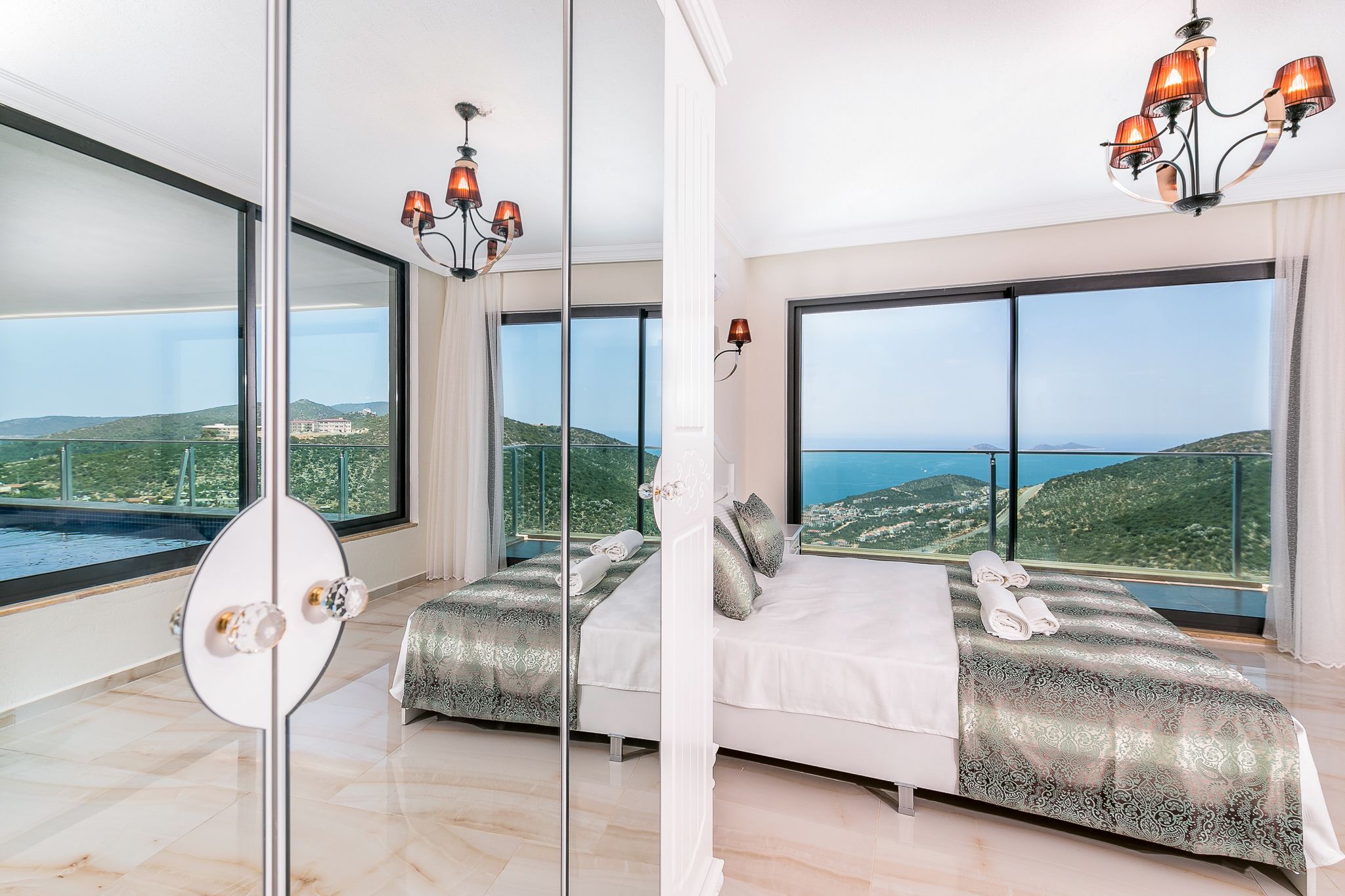 A bedroom with a large bed, a glass partition, and a view of the sea.