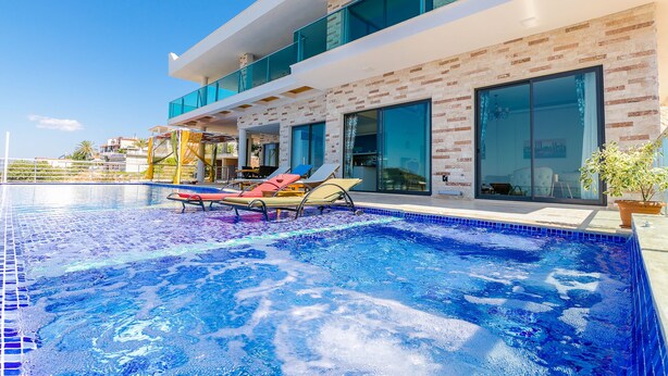 A modern poolside area with a clear blue pool, lounge chairs, and a contemporary building with large windows and a brick facade.