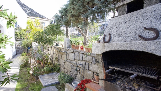 A stone-built outdoor kitchen with a grill, surrounded by potted plants and a stone pathway. - Appartamento La Posta Pomonte (Marciana)