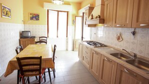 A kitchen with wooden cabinets, a dining table with chairs, a gas stove, and a sink. - Appartamento La Posta Pomonte (Marciana)