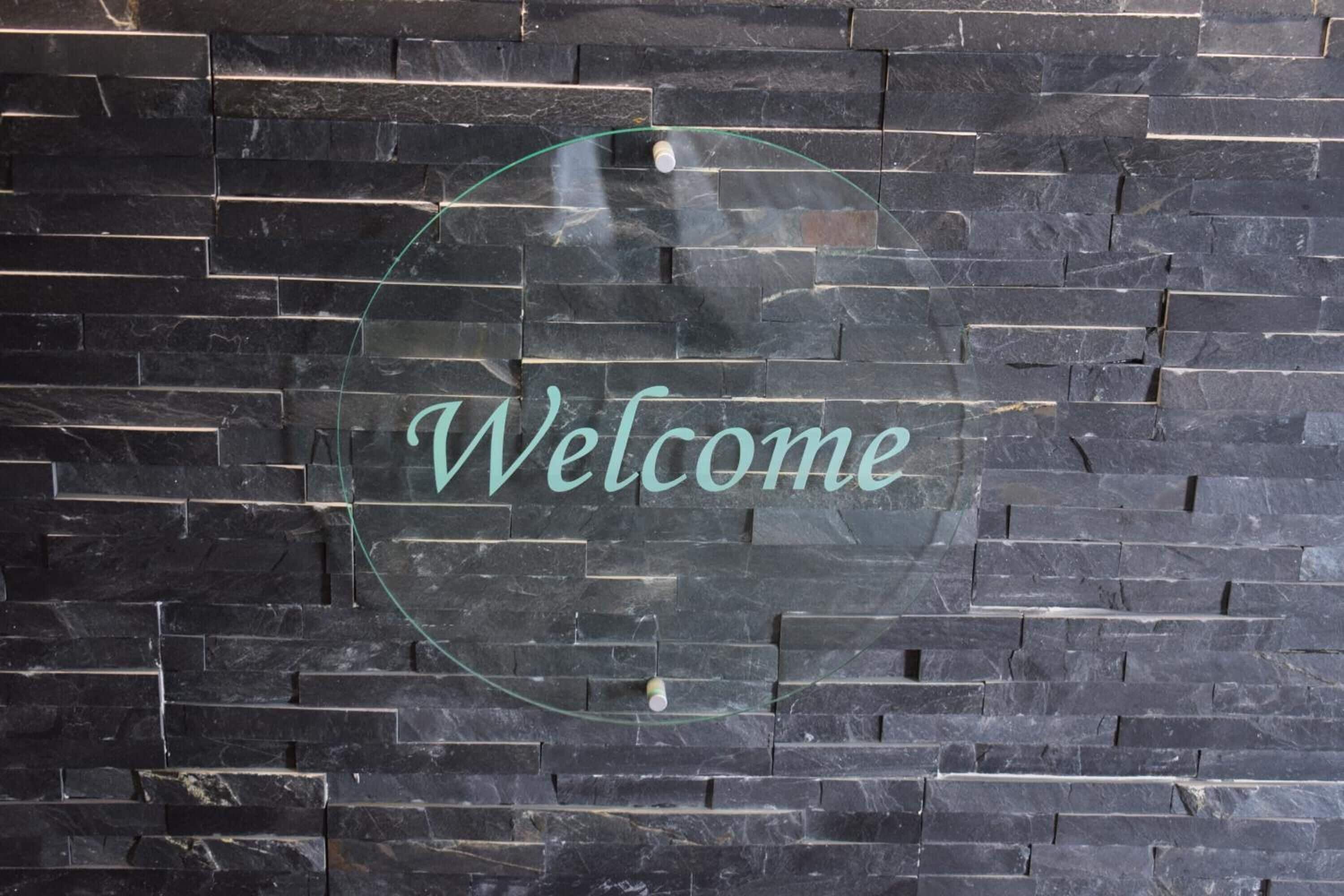A welcome sign with the word "Welcome" on a dark stone wall.