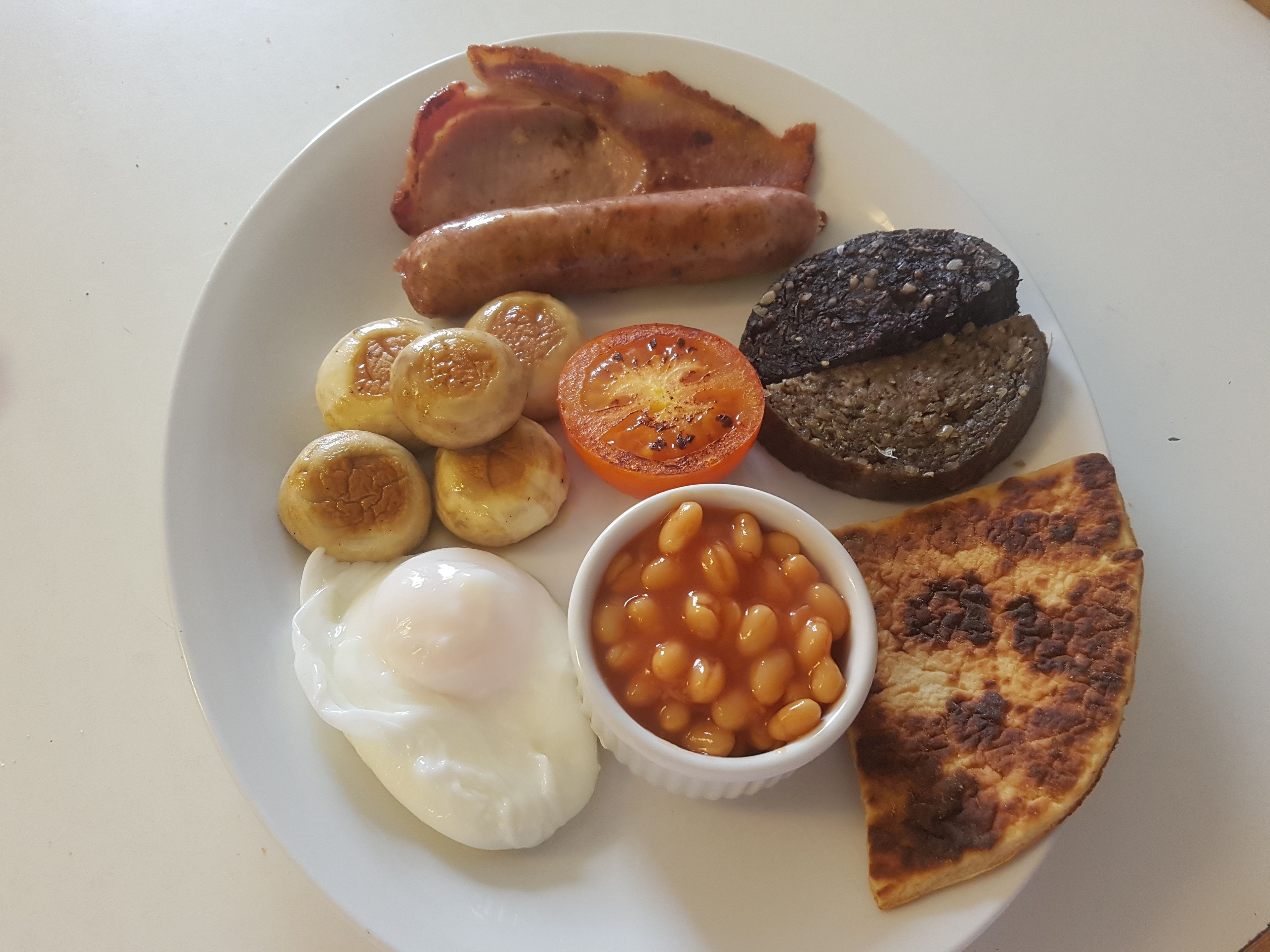 Prato de comida de café da manhã com bacon, linguiça, ovos, feijão cozido, tomate e torradas.