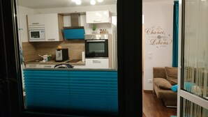Una cocina moderna con armarios blancos y azules, microondas, horno y lavamanos. Hay una encimera azul y una pared con una frase decorativa.