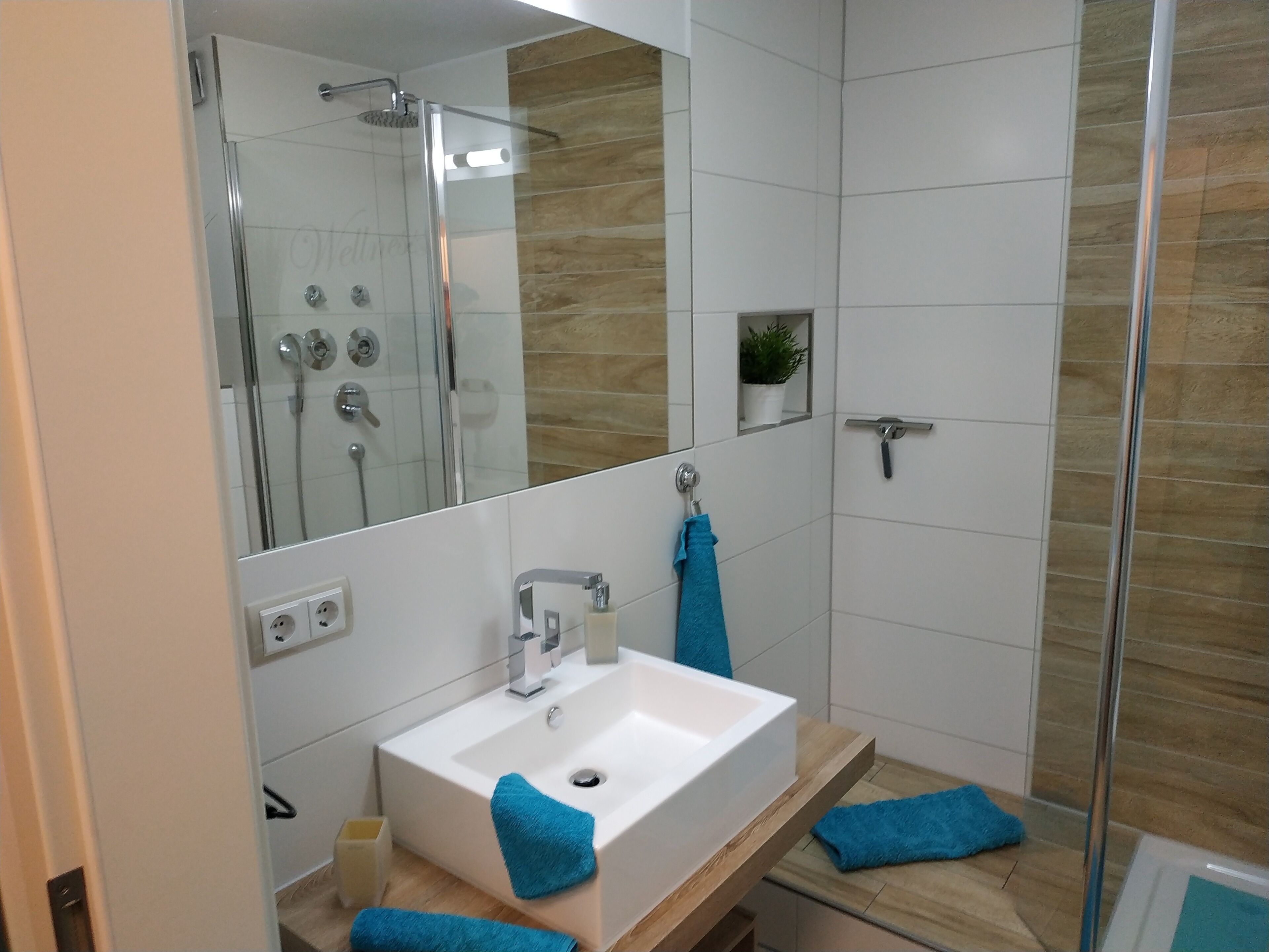 A modern bathroom with a glass shower enclosure, a white sink, and a wooden vanity.