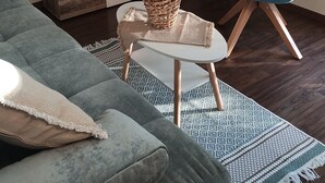 Una sala de estar con un sofá gris, un sillón azul, una mesa de centro con un jarrón, un televisor en la pared y un mueble de madera.