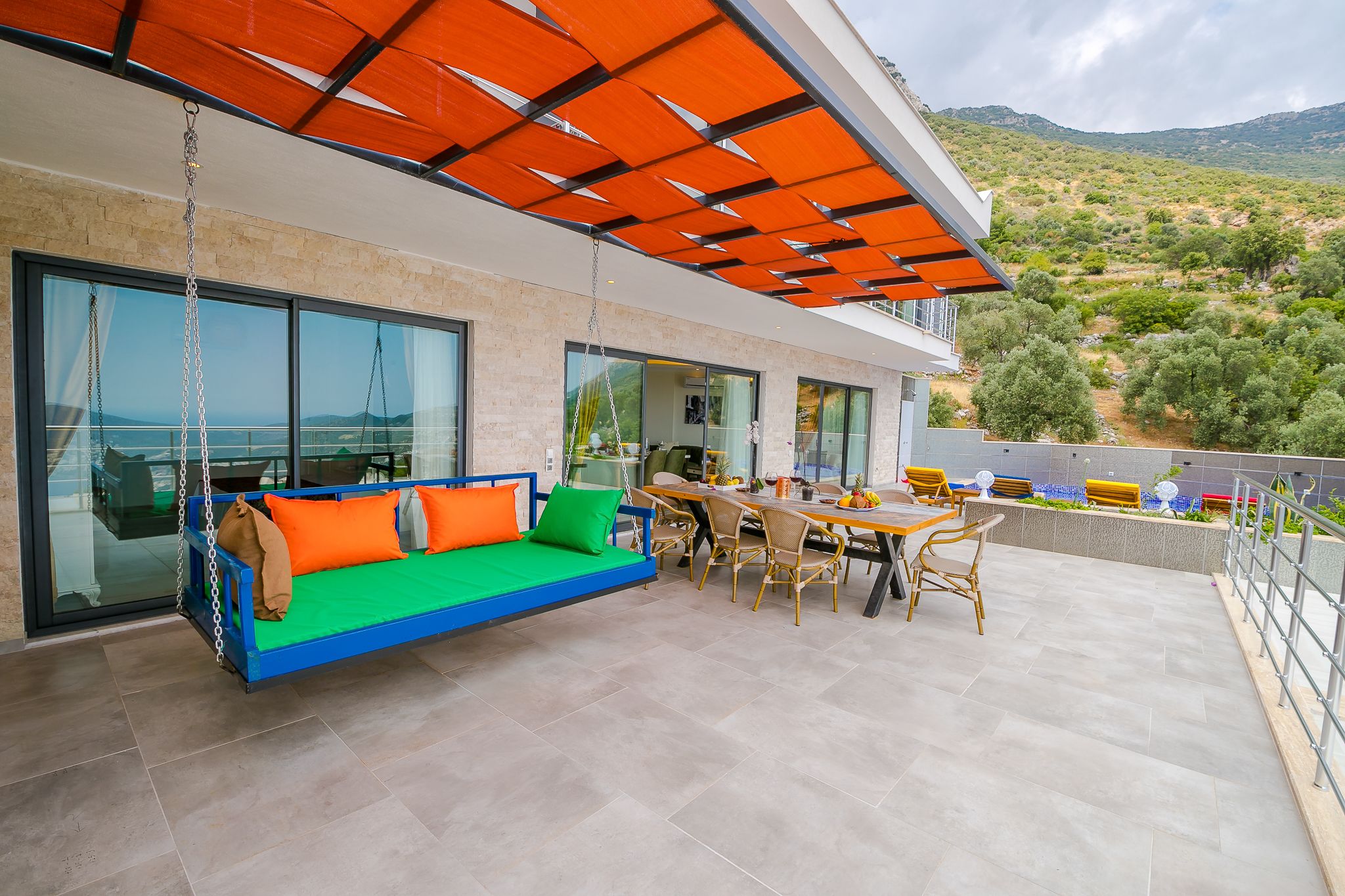 A modern outdoor living area with a swing sofa, dining table, and chairs, overlooking a scenic landscape.