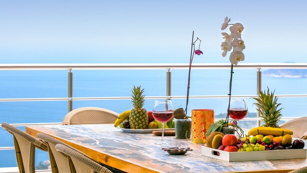 A table with fruits, a wine glass, and a decorative orchid on a balcony with a view of the ocean. - Villa Nature - Hill Villas Kalkan (Kas)