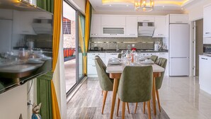 A modern kitchen with white cabinets, a dining table set for four, and a large window. - Villa Nature - Hill Villas Kalkan (Kas)