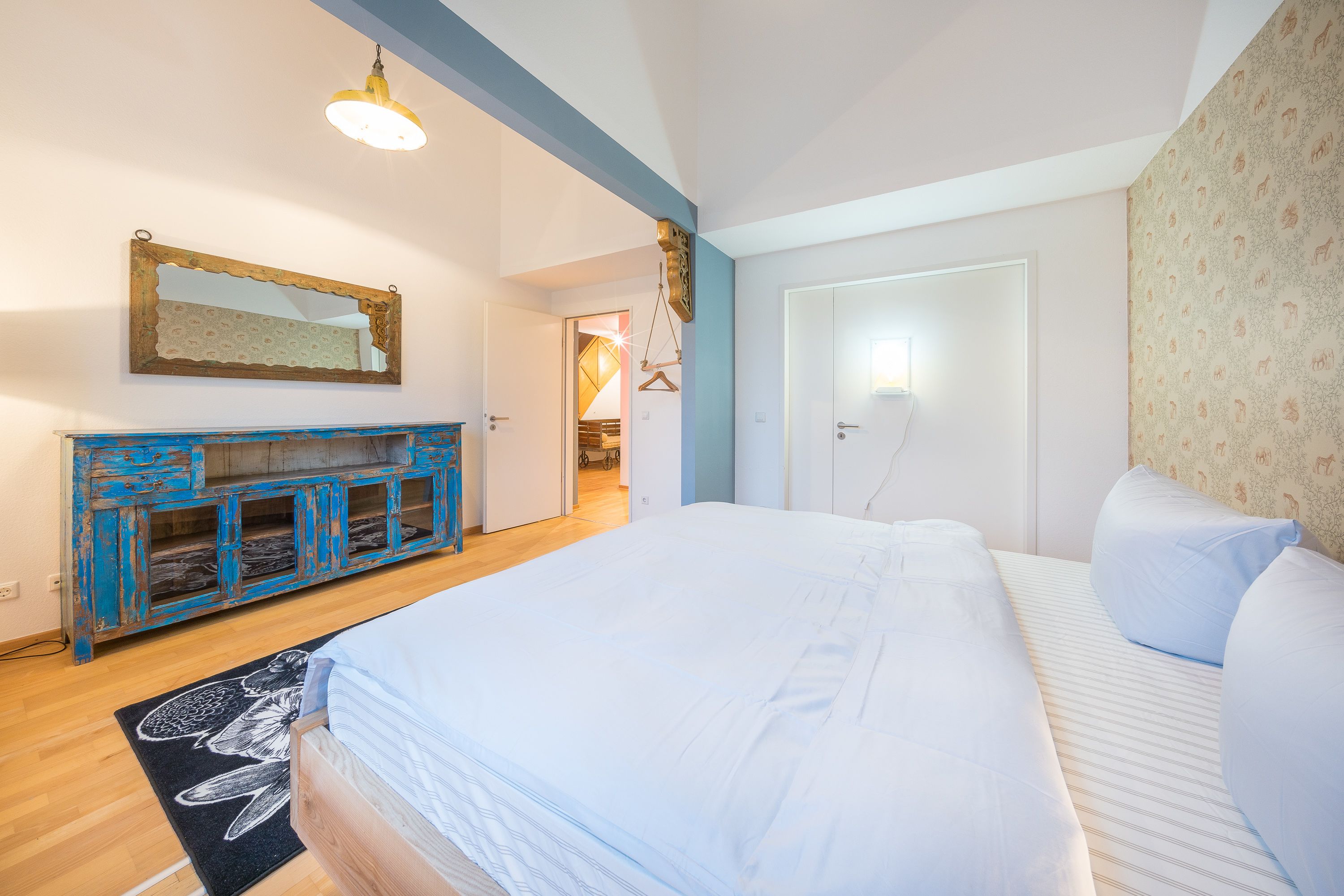 A bedroom with a large bed, a dresser, a mirror, and a door leading to another room.