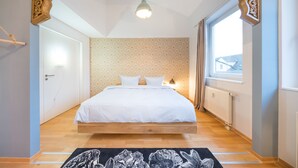 Un dormitorio con cama de madera, papel tapiz estampado, ventana con cortinas y lámpara colgante.