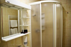 Un baño con espejo, toallero, repisas y cabina de ducha.