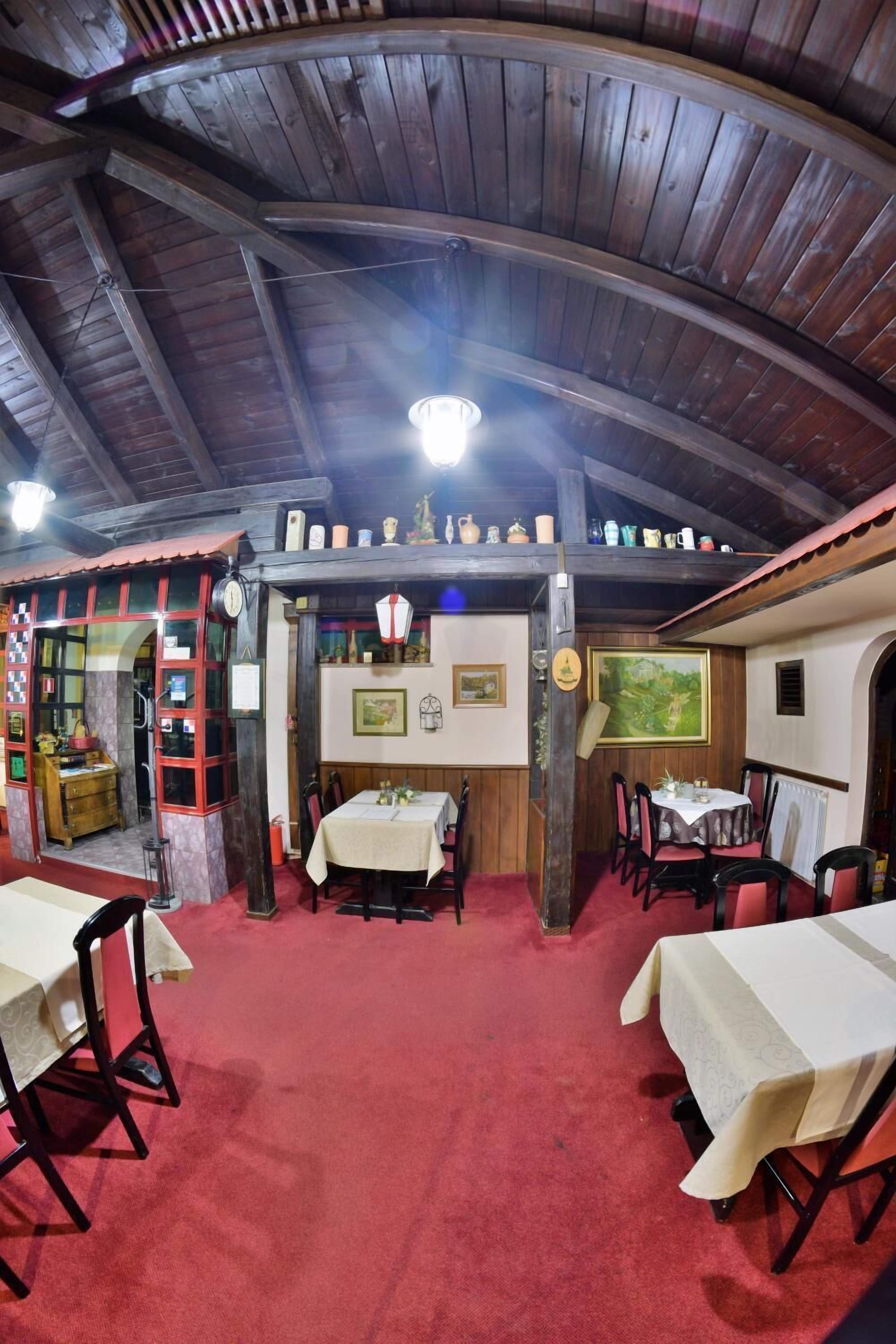 A rustic dining area with wooden beams, red carpet, and tables set for dining.