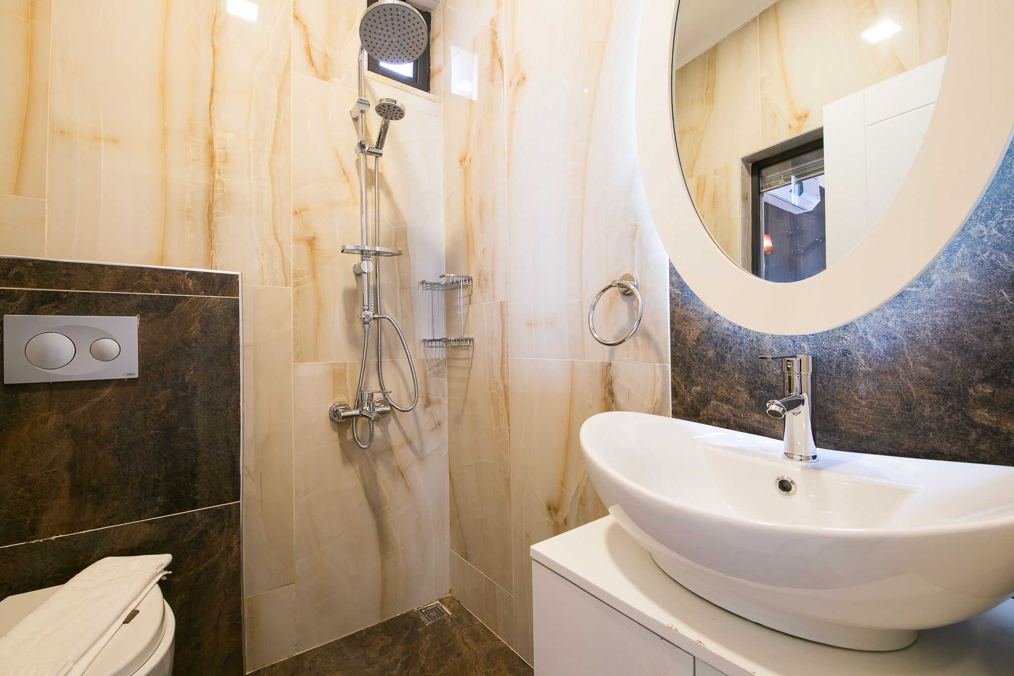 Un baño moderno con un lavamanos grande, una ducha con cabezal de ducha manual y un inodoro.