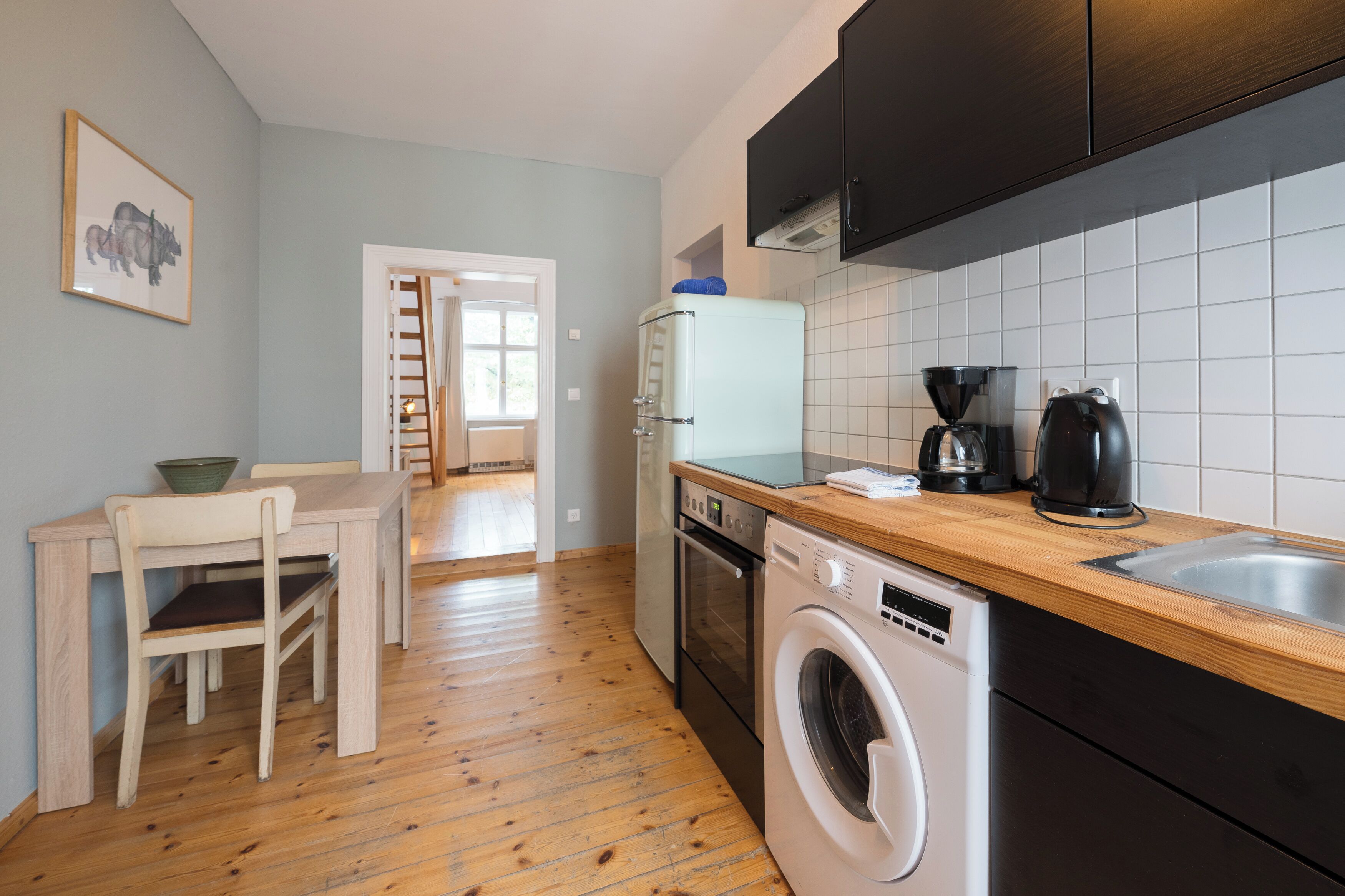 A compact kitchen with a wooden countertop, a washing machine, a coffee maker, and a refrigerator.